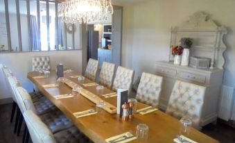 a long wooden dining table set with plates , wine glasses , and napkins in a room with white walls and large windows at The Ship Inn