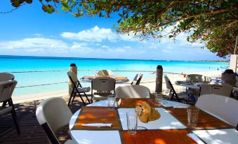 a restaurant with wooden tables and chairs , white tablecloths , and a view of the ocean at Travellers Beach Resort