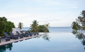 a large swimming pool surrounded by lounge chairs , with palm trees and the ocean in the background at Seanery Beach Resort