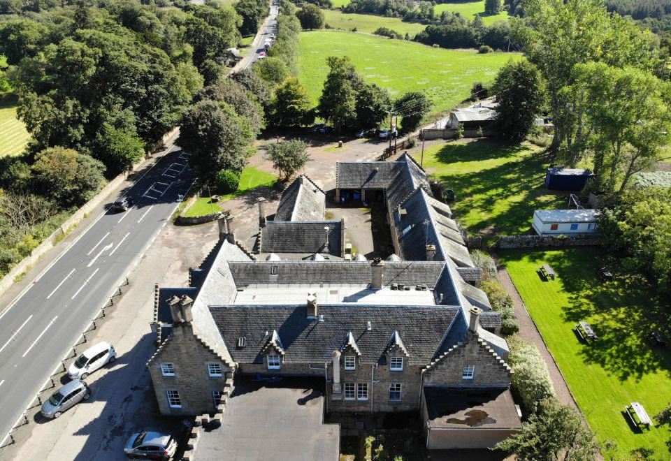 an aerial view of a large stone building surrounded by a lush green field , with a car parked in front of it at The Stair Arms Hotel