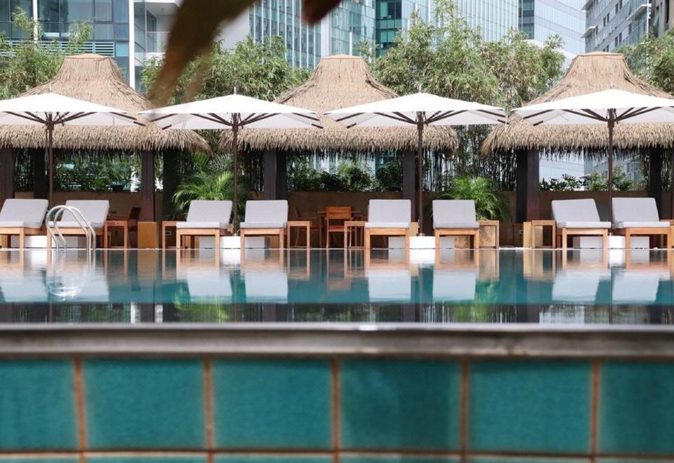 a large outdoor pool surrounded by lounge chairs and umbrellas , with people enjoying their time in the water at Grand Hyatt Manila