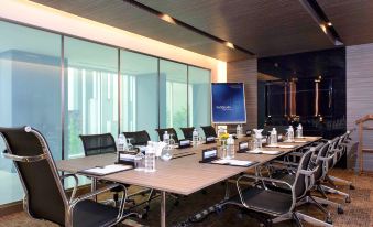 a large conference room with a long table , multiple chairs , and a screen in the background at Novotel Bangkok Impact