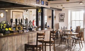 a bar with wooden tables and chairs , a beer tap on the counter , and framed pictures on the walls at The Old Success Inn