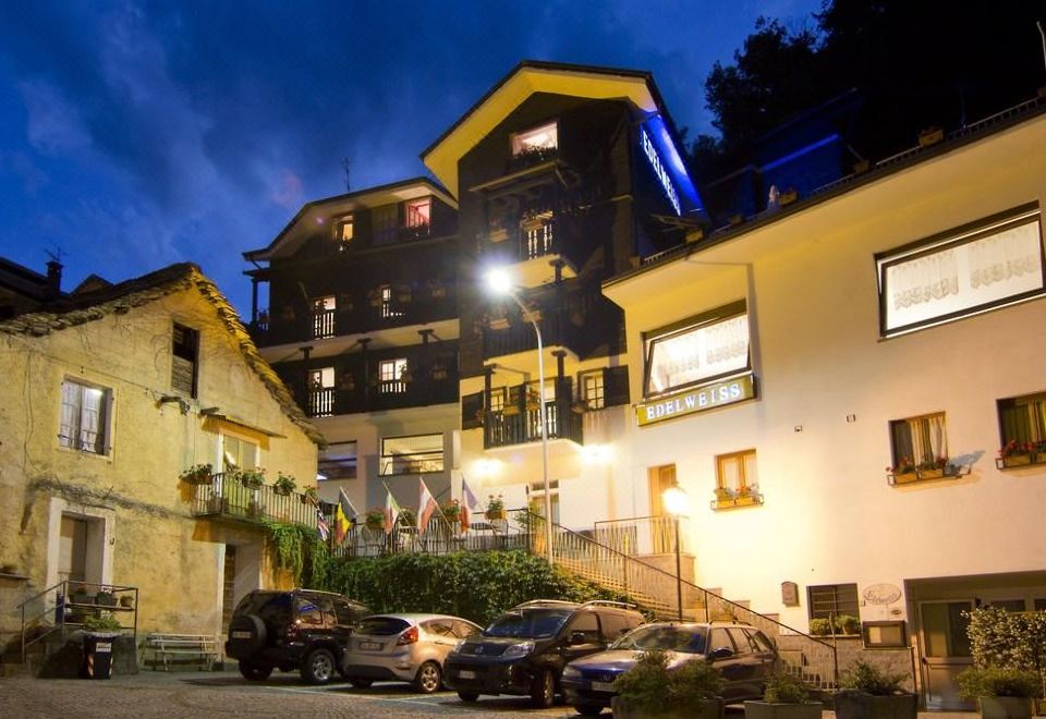 a large building with multiple stories and balconies is lit up at night , surrounded by cars parked on the street at Hotel Edelweiss