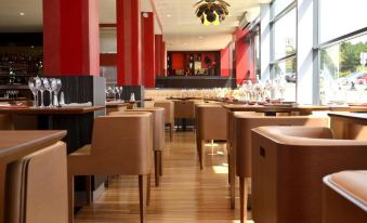 a restaurant with wooden tables and chairs , red walls , and a bar area in the background at Le Grand Hotel