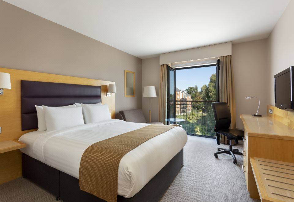 a hotel room with a king - sized bed , a desk , a chair , and a television . the room has a balcony overlooking a city at Holiday Inn London - Brentford Lock