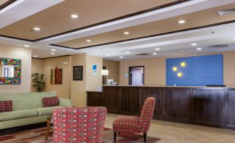 a hotel lobby with a check - in desk , two chairs , and a tv . also a refrigerator in the room at Holiday Inn Express Newington - Hartford