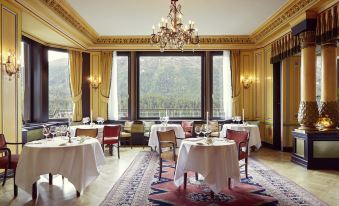 a dining room with a table set for a meal , surrounded by chairs and a chandelier at Badrutt's Palace Hotel St Moritz