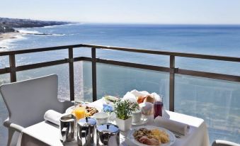 a table is set with breakfast items and a view of the ocean from a balcony at Hotel Estoril Eden