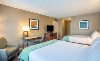a hotel room with two beds , a desk , and a flat - screen tv , all set against a white background at Holiday Inn South Kingstown (Newport Area)