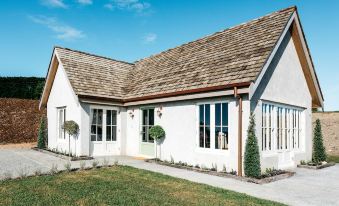 a white house with a wooden roof and large windows is surrounded by green grass at Mudbrick Cottages