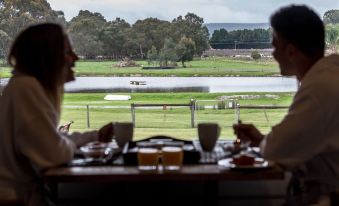 a man and a woman are sitting at a dining table , enjoying a meal while looking out the window at The Swan Valley Retreat