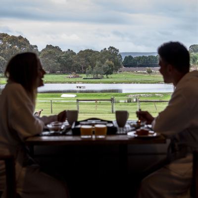 a man and a woman are sitting at a table with cups of tea , enjoying the view of the field at The Swan Valley Retreat