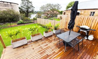 a wooden deck with a dining table , chairs , and umbrellas overlooks a grassy area and trees at Cockatoo Island Accommodation