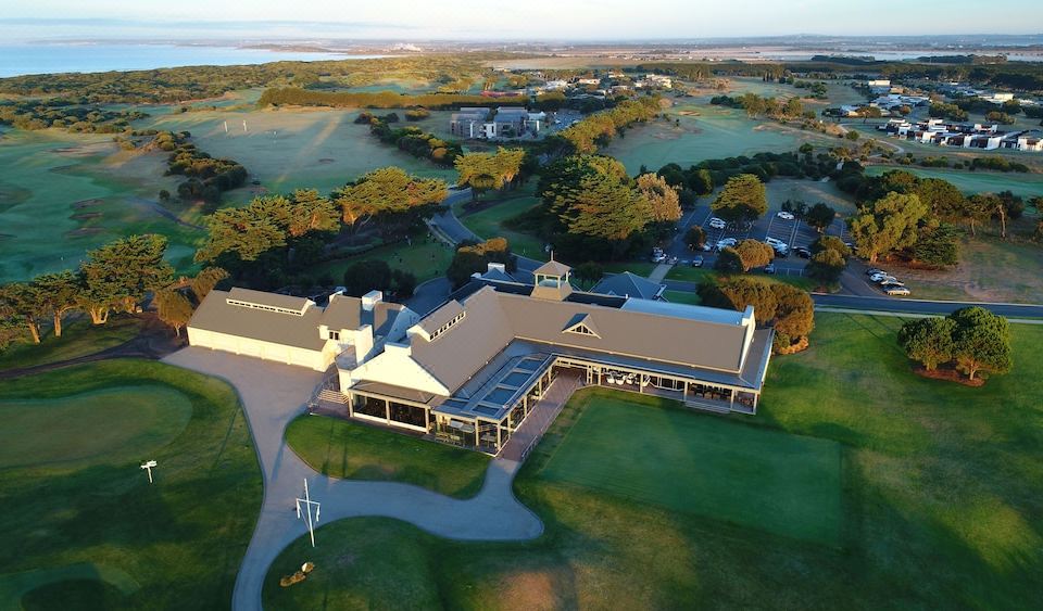 an aerial view of a large building surrounded by green grass , trees , and a body of water at 13th Beach Golf Lodges