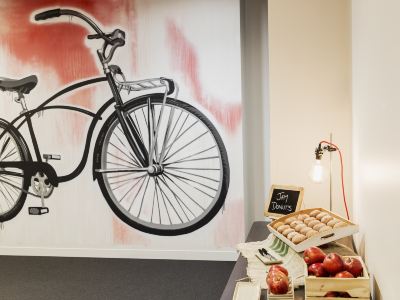 a black bicycle is displayed against a wall with an image of the bicycle , and fruit in a basket at Ibis Melbourne Hotel and Apartments