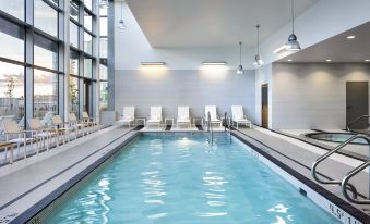 an indoor swimming pool surrounded by white lounge chairs , with several people enjoying their time in the pool at Element Vancouver Metrotown