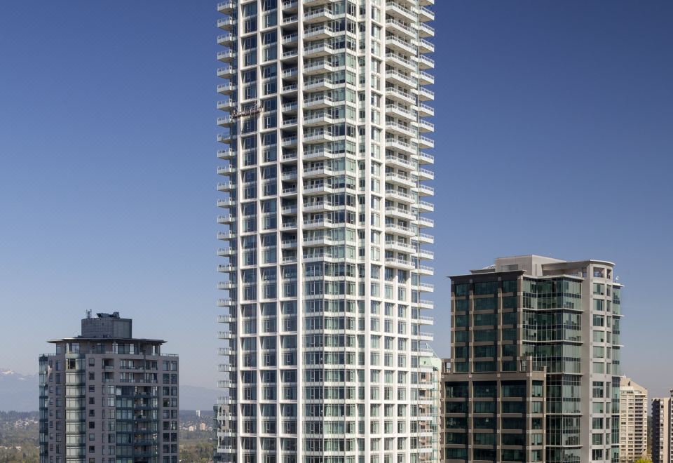 a tall white skyscraper with many windows is surrounded by other tall buildings in a city at Element Vancouver Metrotown