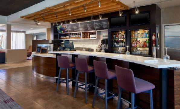 a modern bar with a long wooden counter and several stools , creating a comfortable atmosphere for patrons at Sonesta Select Raleigh Durham Airport Morrisville