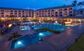 a large outdoor swimming pool surrounded by a hotel building at night , with lights illuminating the area at Sheraton Kauai Coconut Beach Resort