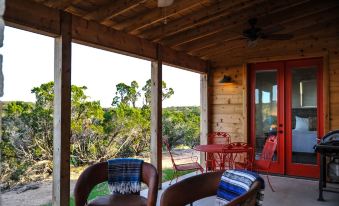 a wooden porch with two chairs and a dining table , surrounded by trees and grass at Hill Country Casitas