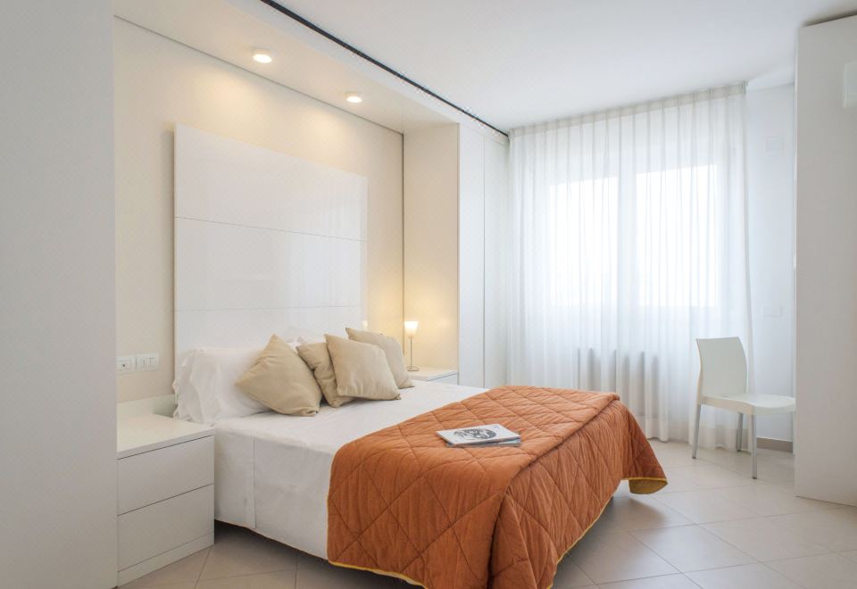a clean , white bedroom with a large bed and an orange comforter , accompanied by two lamps on either side of the bed at Nautilus