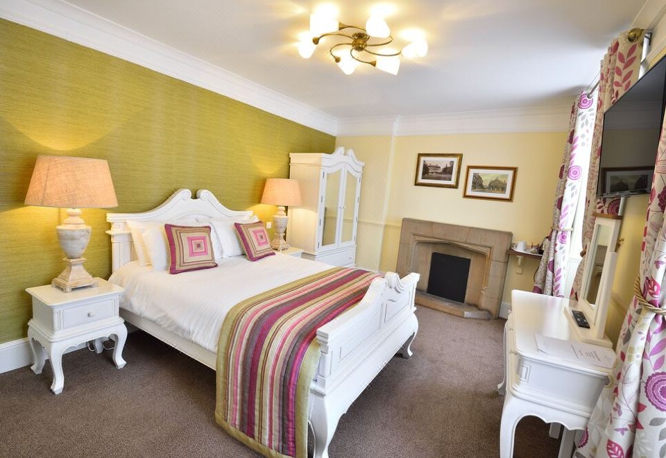 a large bedroom with a white bed , a fireplace , and a dresser in the corner at The George Hotel
