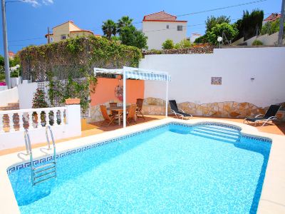 a beautiful outdoor swimming pool area with blue water , white walls , and lush greenery surrounding a white house at Joli Joli Photo