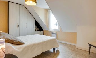 a cozy bedroom with a white bed , hardwood floors , and a slanted ceiling , as well as a window and a rug at L'Olivier