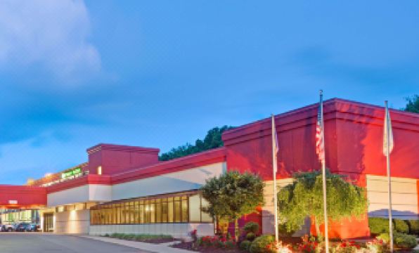 a large building with a red facade and green windows is surrounded by trees and bushes at Wyndham Garden Pittsburgh Airport