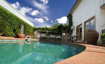 a large , kidney - shaped swimming pool surrounded by a patio area with potted plants and a house in the background at Admiralty Inn