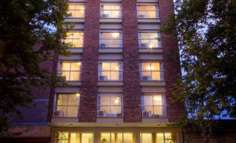 a tall brick building with a balcony and lit windows is surrounded by trees at night at Hotel Royal