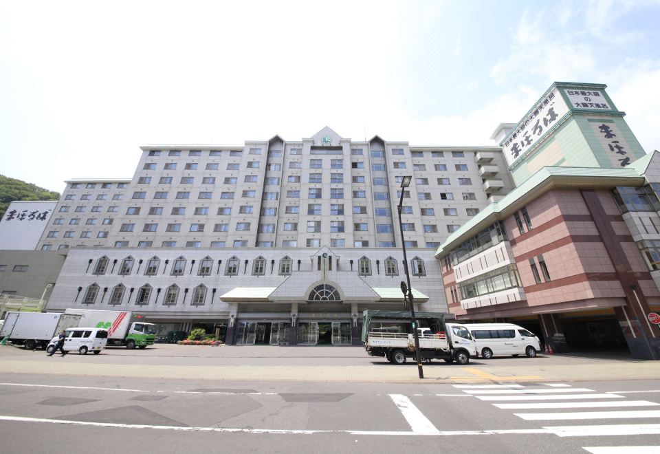 a large , white hotel building with multiple balconies and a car parked in front , set against a clear sky at Hotel Mahoroba