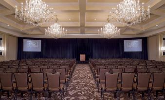 a large conference room with rows of chairs arranged in a symmetrical pattern , facing a podium and two chandeliers hanging from the ceiling at Grand Hyatt Denver