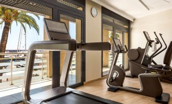 a well - equipped gym with various exercise equipment , including treadmills and weightlifting machines , near large windows that offer views of the ocean at Riviera Marriott Hotel la Porte de Monaco
