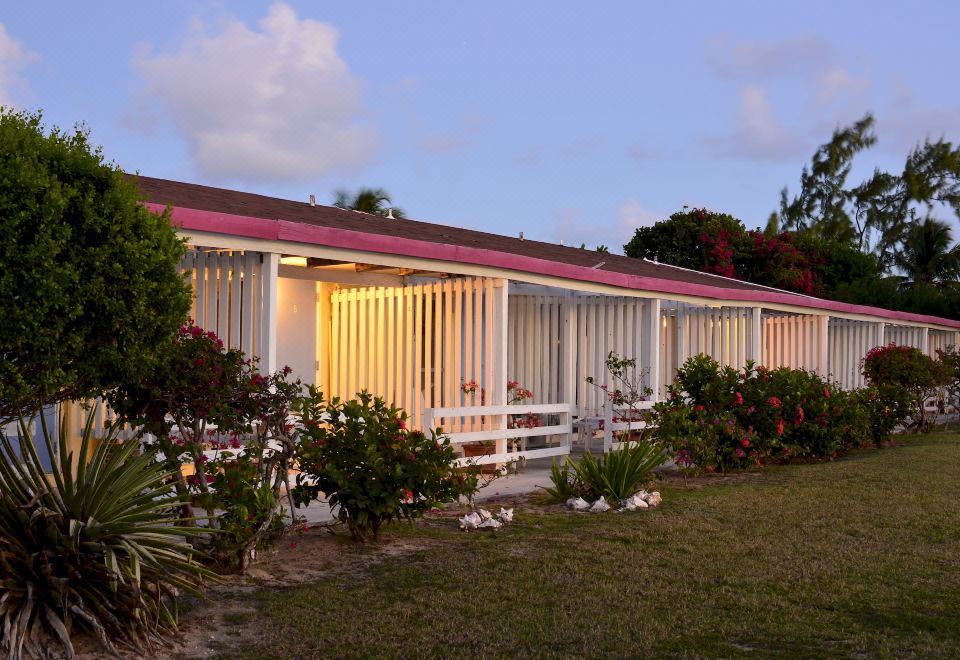 a modern , white - framed house with a pink roof and large windows is surrounded by lush greenery at Anegada Reef Hotel