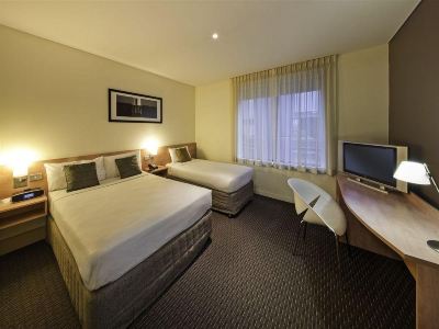 a hotel room with two beds , a desk , and a tv , all neatly arranged on a carpeted floor at Ibis Melbourne Hotel and Apartments
