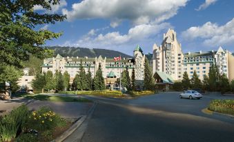 a large hotel with a traditional canadian flag on top is surrounded by trees and mountains at Fairmont Chateau Whistler