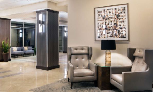 a modern living room with gray chairs , a wooden side table , and a large framed artwork on the wall at Sheraton Suites Chicago Elk Grove