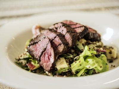 a white bowl filled with a delicious steak salad , accompanied by a fork and knife at Ibis Melbourne Hotel and Apartments