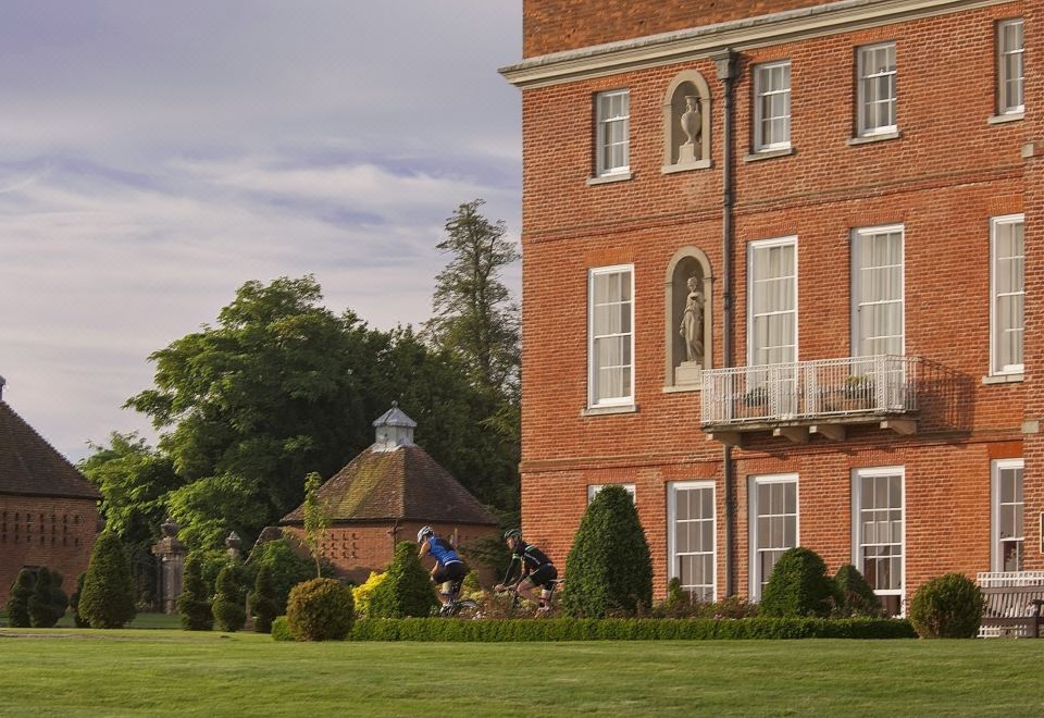 a large red brick building surrounded by a lush green lawn , with a group of people gathered in front of it at Four Seasons Hotel Hampshire