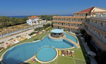 an outdoor swimming pool surrounded by a hotel , with people enjoying their time in the pool at Bayside Hotel Katsaras