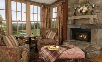 a cozy living room with a fireplace , chairs , and a table , all set against the backdrop of a beautiful view at Windham Hill Inn