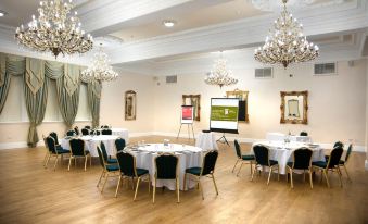 a well - decorated banquet hall with tables and chairs set up for a formal event , along with a projector screen and chandeliers hanging from at Doxford Hall Hotel and Spa