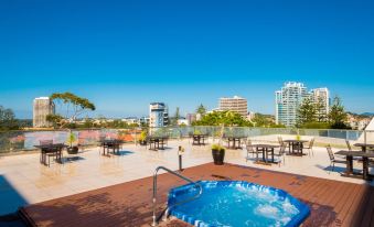 a rooftop with a hot tub and dining area , surrounded by trees and buildings in the background at Greenmount Beach House