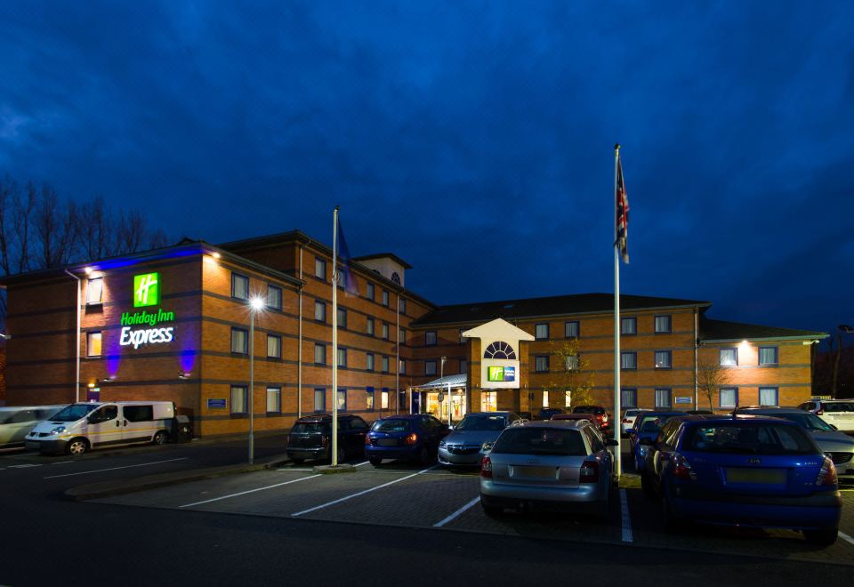 a holiday inn express hotel at night , with its logo visible and parking lot filled with cars at Holiday Inn Express Droitwich Spa