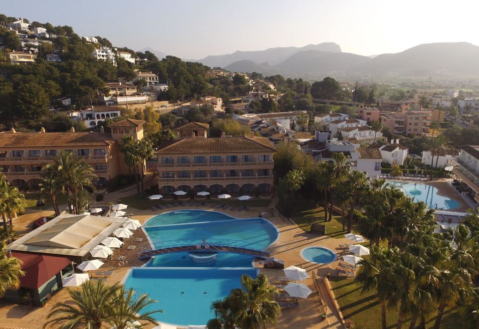a large hotel with a swimming pool surrounded by palm trees and mountains in the background at Mon Port Hotel & Spa