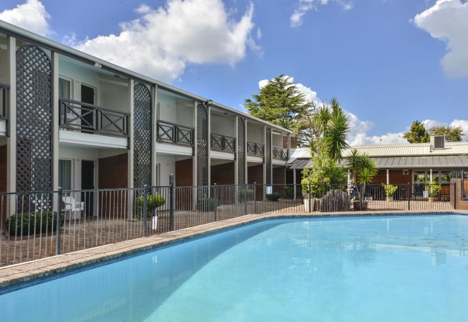 a large swimming pool is surrounded by a building with balconies and trees , under a blue sky with clouds at Poenamo Hotel