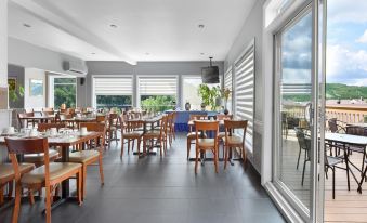 a large , empty restaurant with wooden tables and chairs is shown through a window overlooking the ocean at Hotel le Versailles