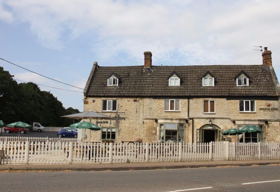 a white picket fence surrounding a brick building , which is situated on the side of the road at The Woolpack Inn